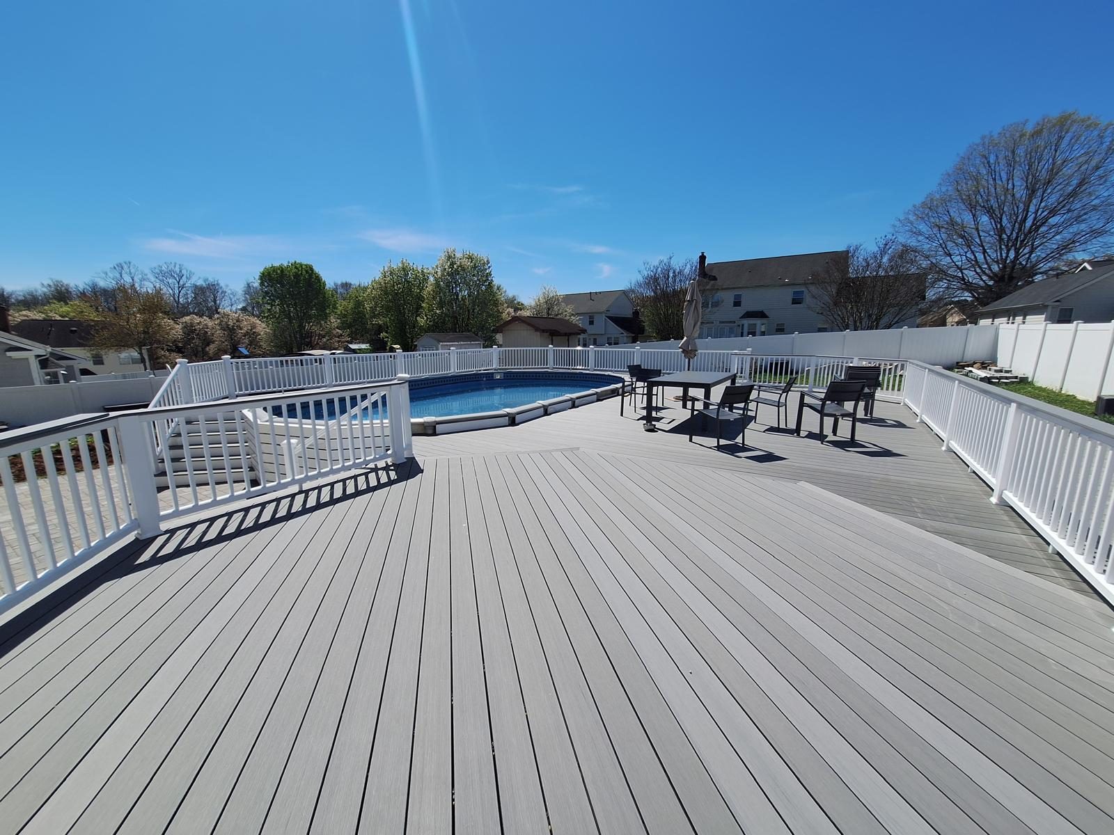 Wide composite deck running beside an above-ground pool, enclosed by white fencing