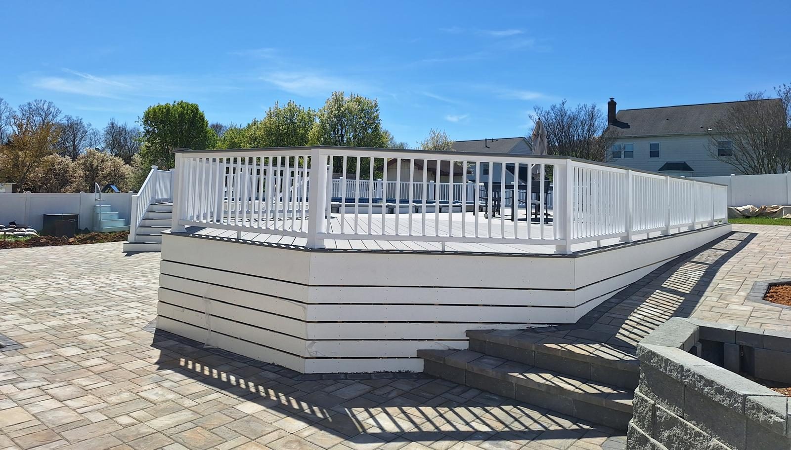 White-skirted pool deck with steps leading down to a paver patio