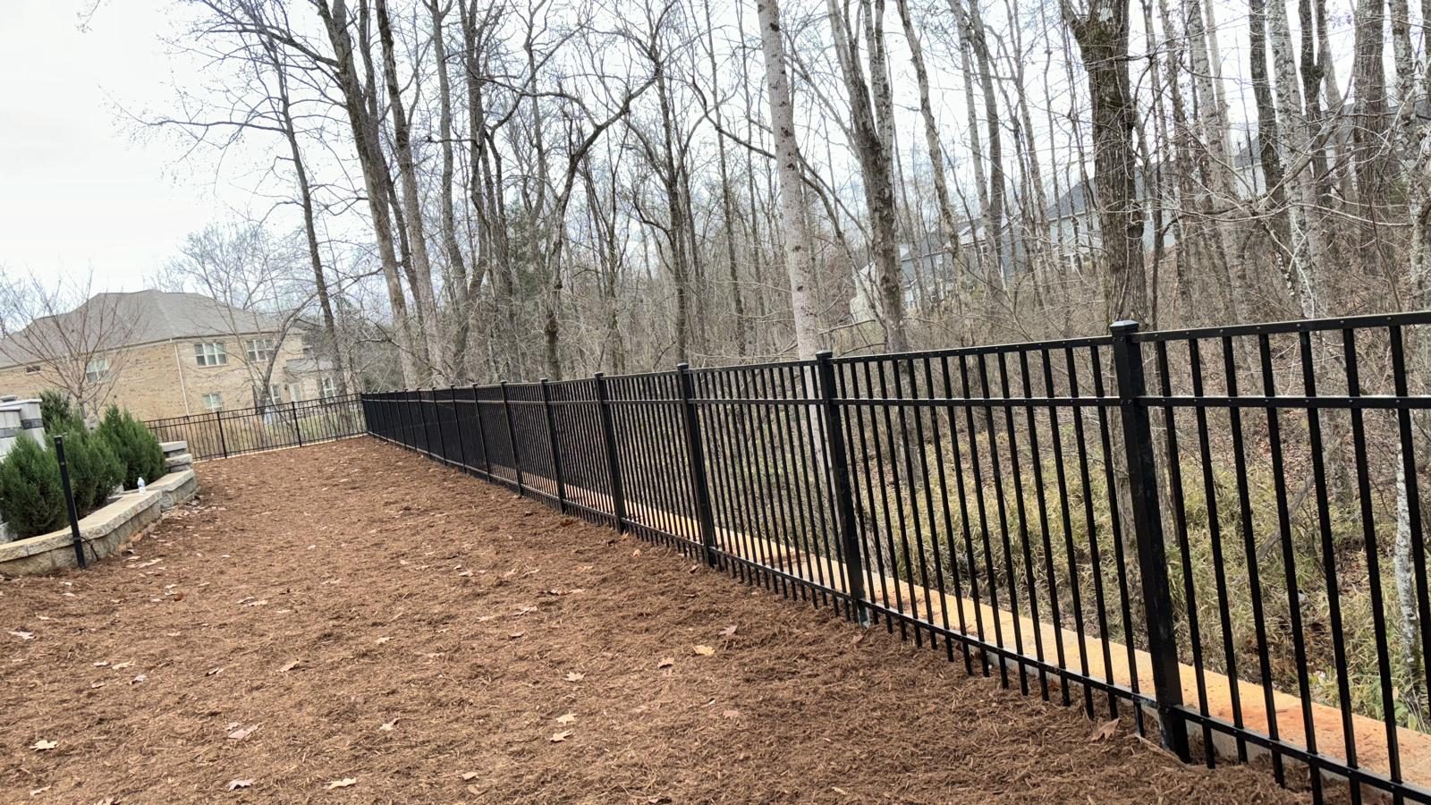 Black aluminium fence running along a wooded property line