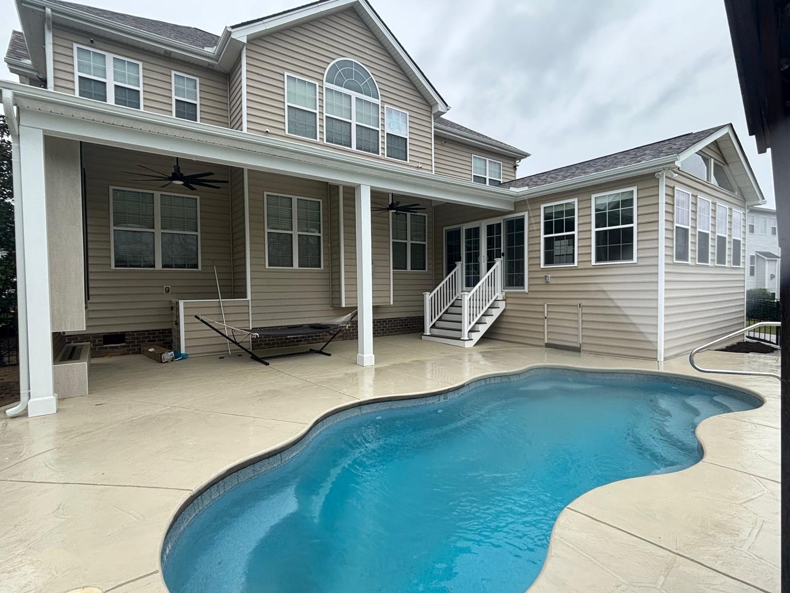 Covered porch across the back of a large home overlooking a curved swimming pool