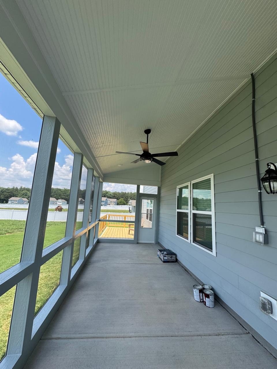 Inside a screened porch looking down its length, with a ceiling fan overhead and a deck beyond