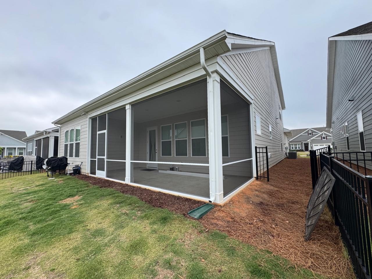 Finished screened porch on a light grey home, bordered by a black metal fence and fresh mulch