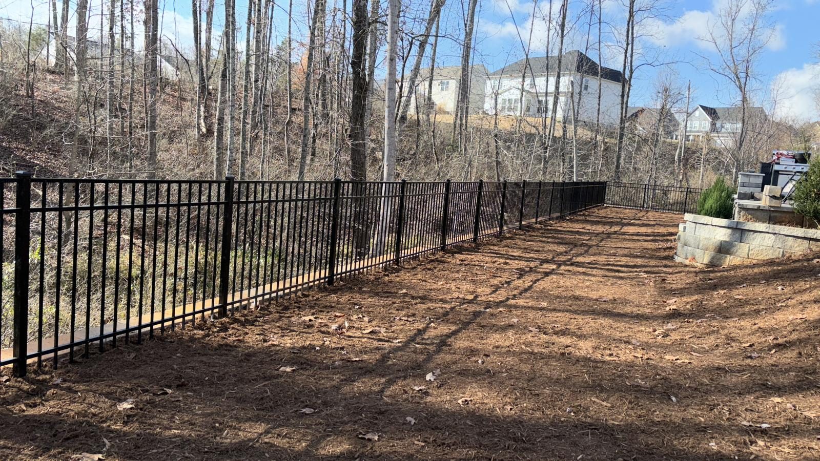 Long run of black aluminium fencing at the edge of a wooded lot