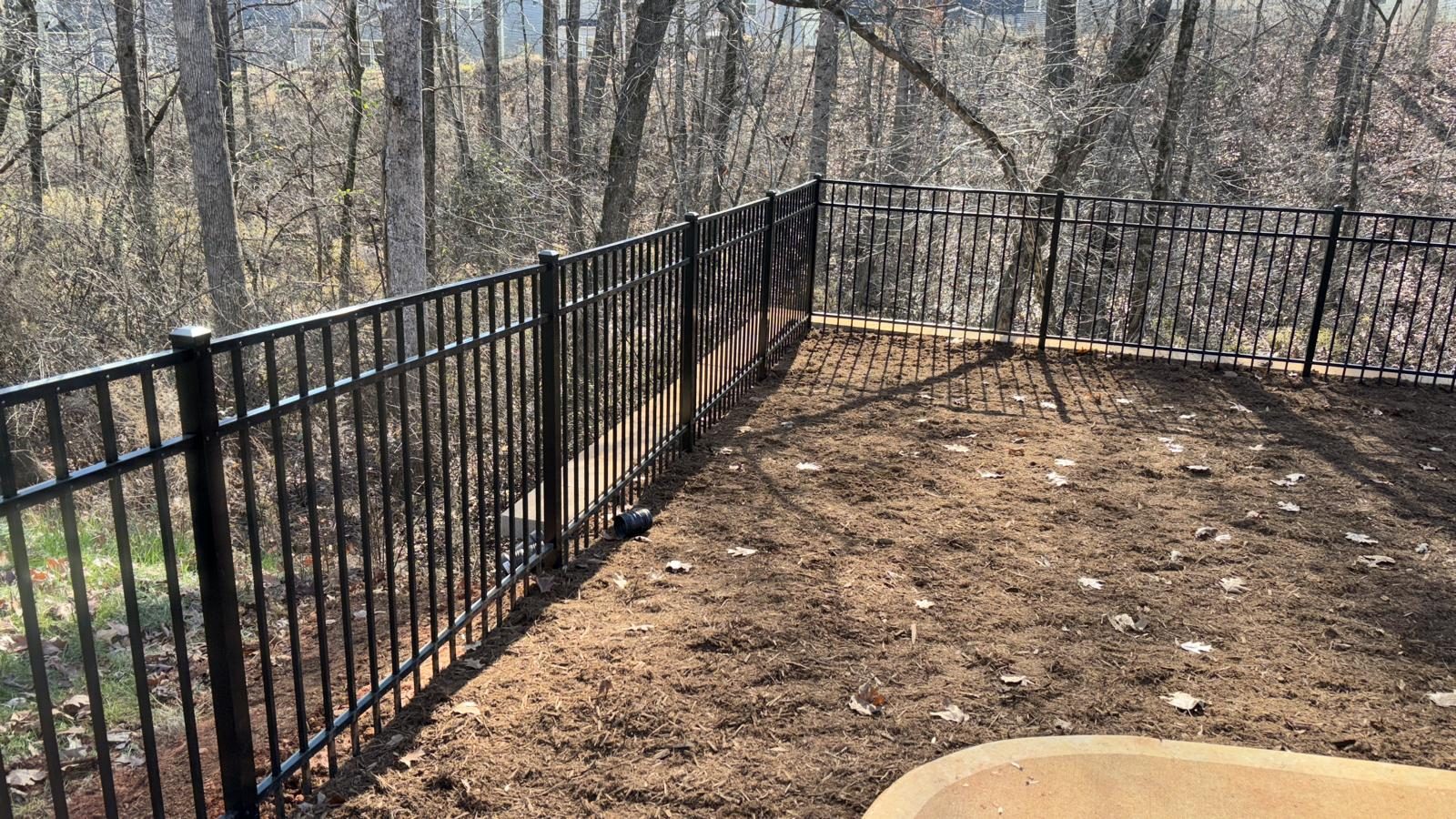 Black aluminium fence enclosing a back garden against woodland