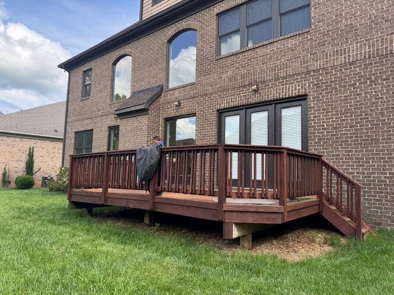 Stained wood deck with a curved railing along the back of a brick home