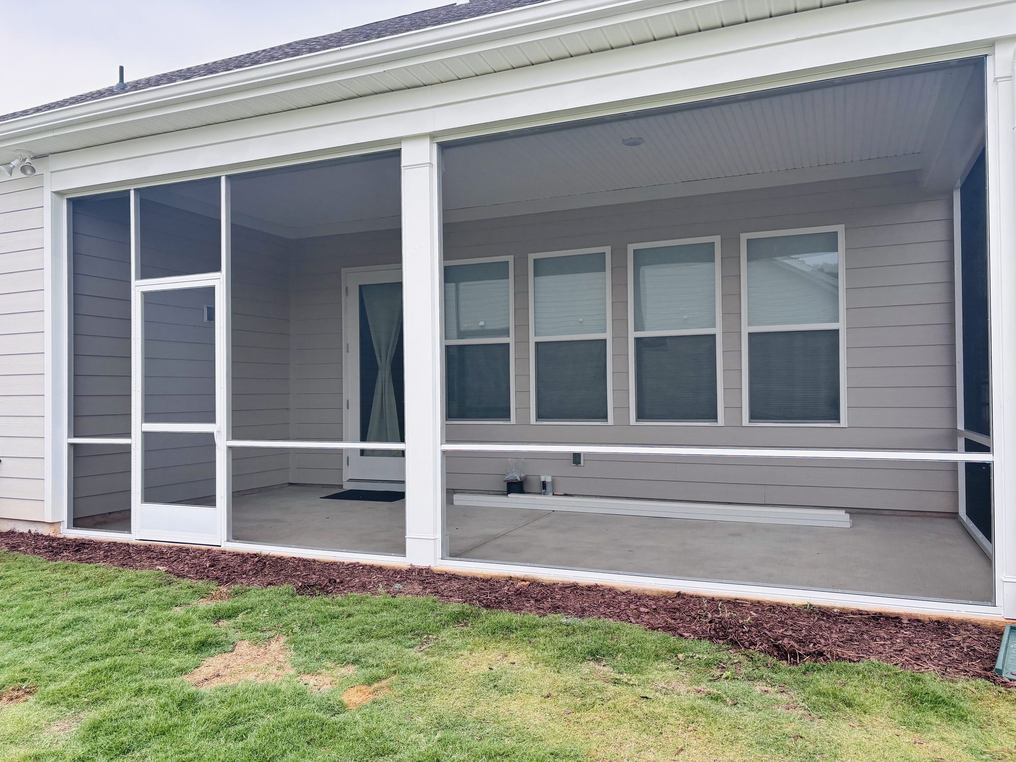 Newly built screened porch with white posts and dark screening on a grey home, with fresh mulch along the foundation
