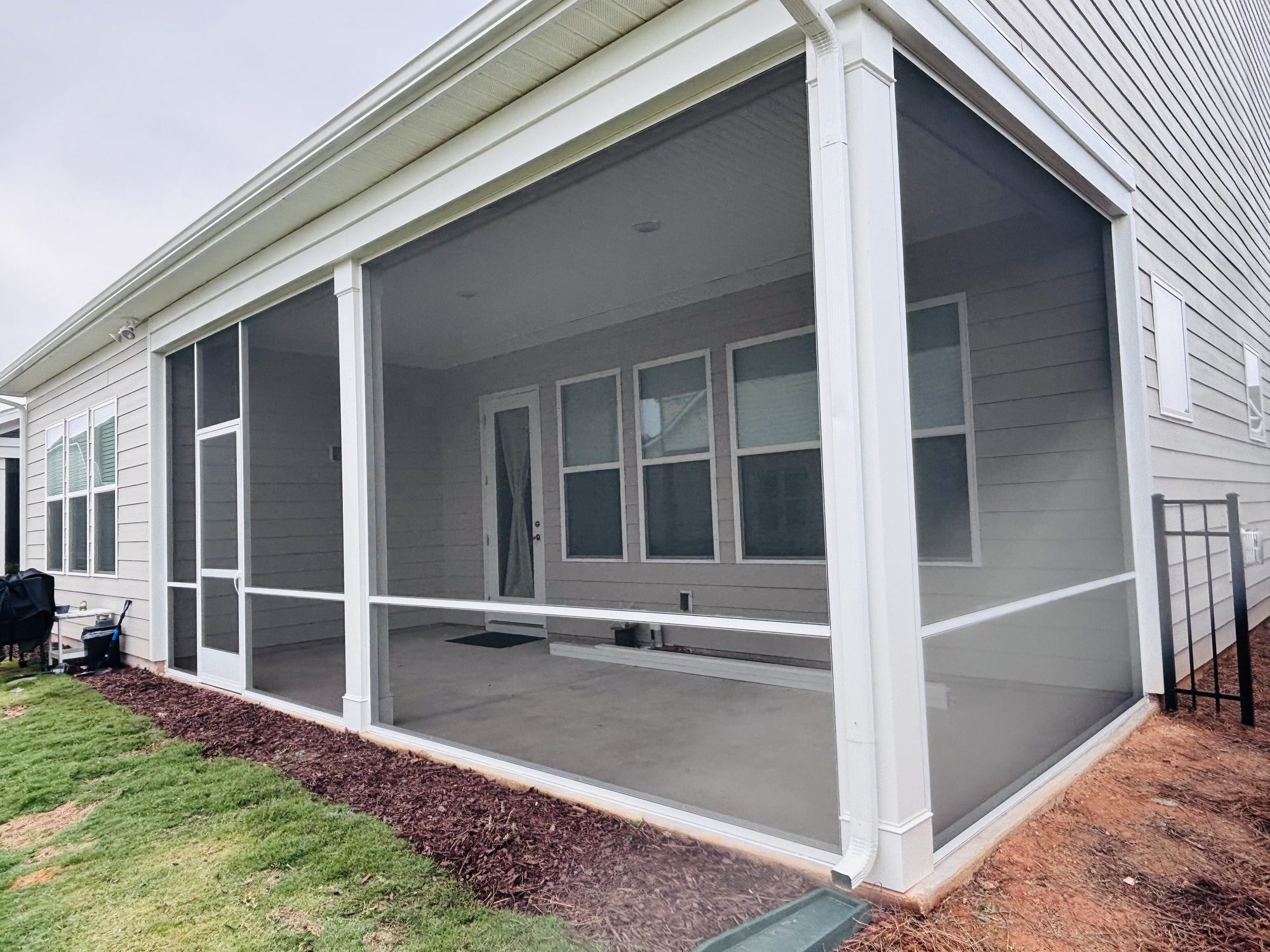 Screened porch seen from the side, showing the full run of screen panels and a concrete floor