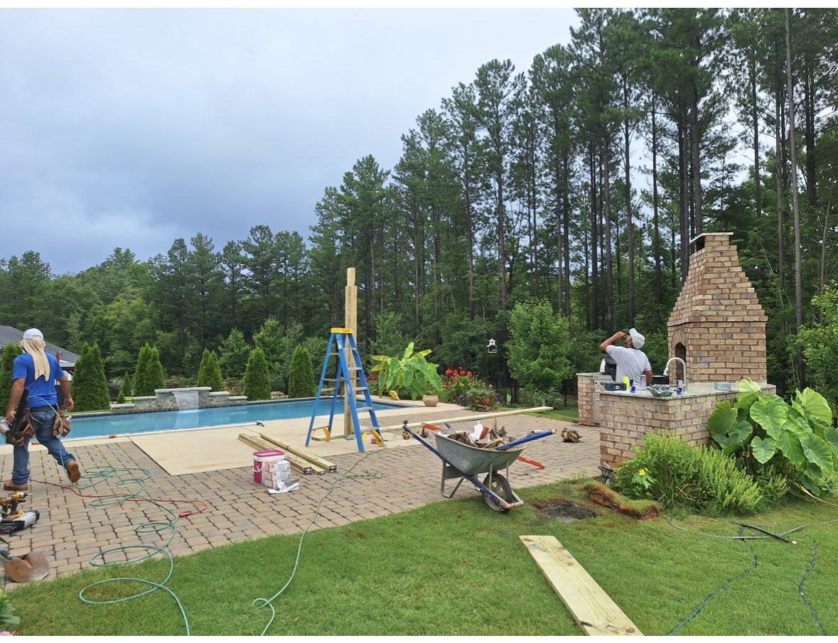 Pergola and brick outdoor fireplace being built beside a swimming pool