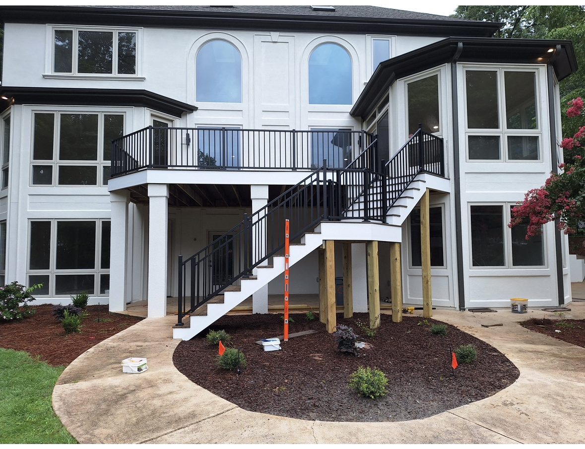 Two-storey deck with black railings and a staircase down to the garden of a white home